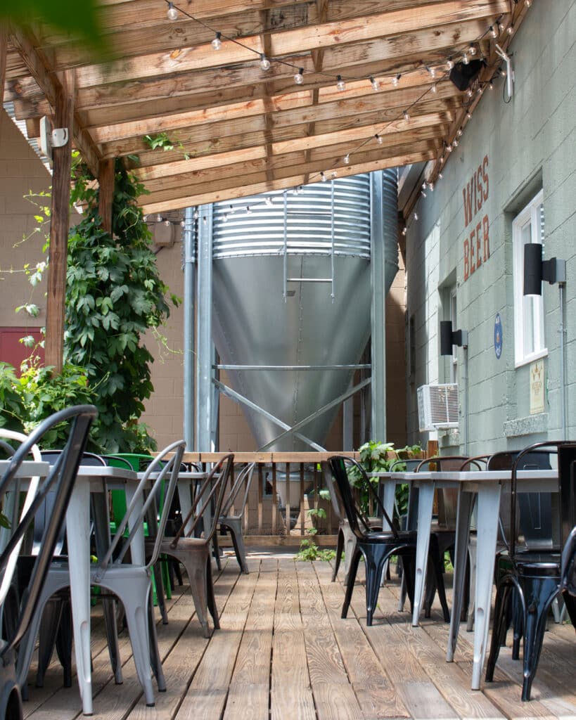 A photo shows the hop deck outdoor sitting area at wissahickon brewing company's east falls location. The space features a deck, covered with growing hop vines. Wissahickon Brewing Company, Philadelphia, pennsylvania, beer, East Falls, Kensington, Maple Glen